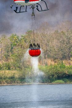 Firefighting helicopter refills water bucket in a pond