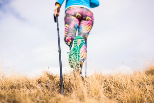 Hiking girl in a mountain meadow. Low angle view of generic sports shoe and legs. Focus on grass. Healthy fitness lifestyle outdoors.