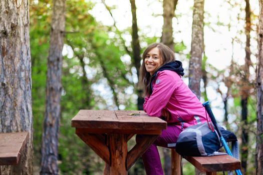 Hiker girl resting on a bench in the forest. Backpacker with pink jacket in nature.