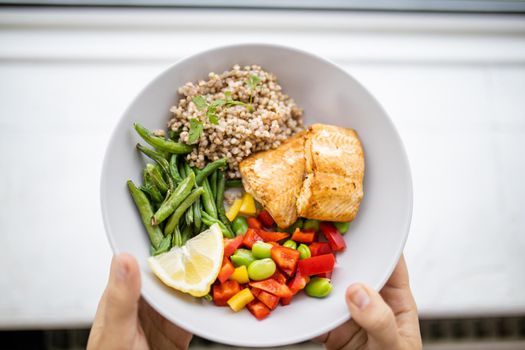 Hands holding salmon and buckwheat dish with green beans