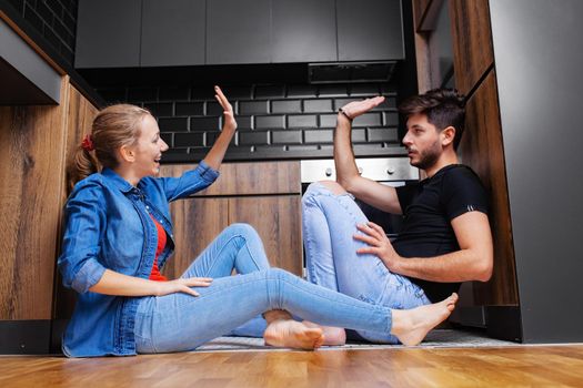 couple giving high five sitting on the floor of a modern kitchen