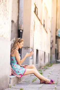 girl sitting on the sidewalk checking her phone