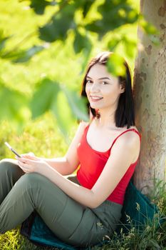 happy dark brown hair girl with her smartphone under a tree