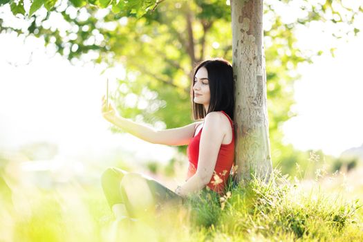 happy dark brown hair girl with her smartphone under a tree
