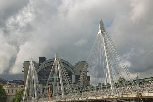 View of the Golden Jubilee Bridges and Charing Cross Station from the South Shore of the River Thames in London on a cloudy Summer day
