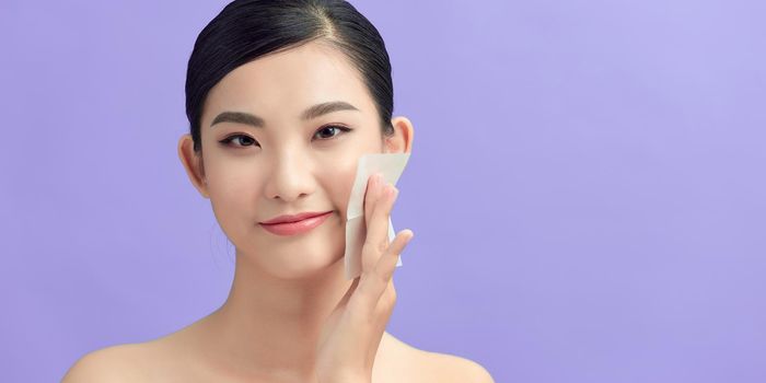 Women with oily skin using oil absorbing sheet on her face