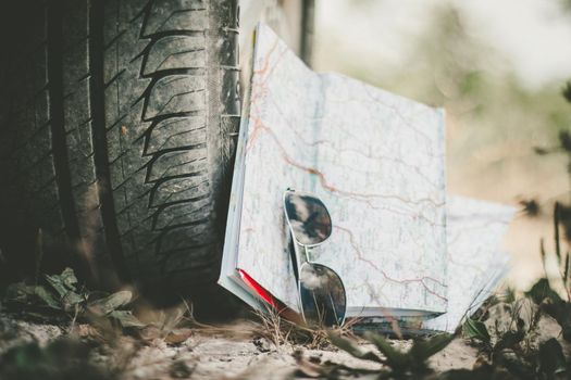 Adventure trip: close of car tyre, sunglasses and road map