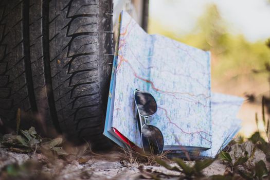 Adventure trip: close of car tyre, sunglasses and road map