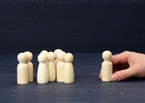 a crowd of wooden figures, opposite the hand is holding one figure. Personnel selection concept, search for talented employees