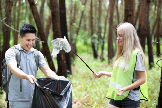 Green volunteering. Optimistic two volunteers holding garbage bag and help picking up trash at park, they're picking up the garbage and putting it in a black garbage bag. ecology protection concept.