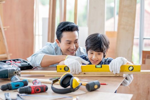 Asian father teach his son to use to for measure and adjust the level of woodwork in their house. Concept of good relationship with hobby or activities in happy family.