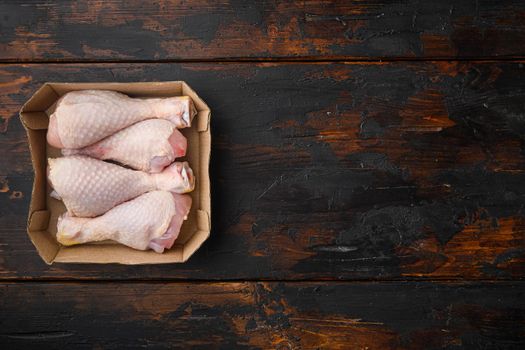 Raw and uncooked chicken drumsticks, in paper Pack, on old dark wooden table, top view flat lay, with copy space for text