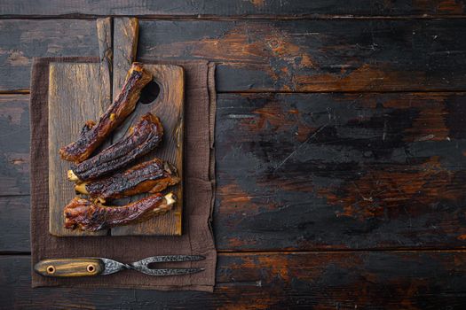 Pork ribs grilled with BBQ sauce and caramelized in honey, on wooden serving board, with barbeque knife and meat fork, on old dark wooden table background, top view flat lay, with copy space for text