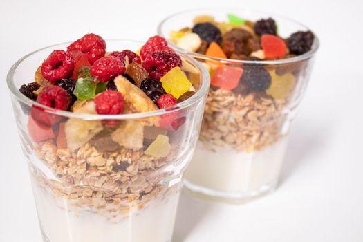muesli dessert with yogurt and candied or dried fruits with raspberries on top in glass isolated on white background. Granola breakfast