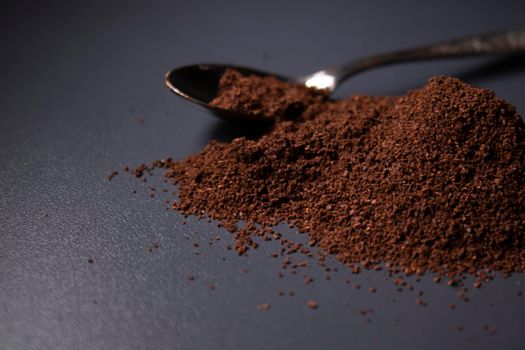 gold teaspoon in a pile of ground or instant coffee on dark background