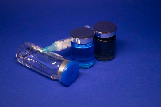 three transparent Vaccine bottle phial with no label, medical syringe injection needle. isolated on blue background. Development of coronavirus vaccine COVID-19. cure. World race in researching