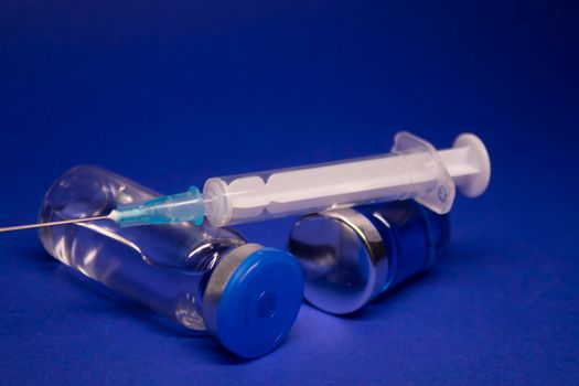 two transparent Vaccine bottle phial with no label, medical syringe injection needle. isolated on blue background. Development of coronavirus vaccine COVID-19. cure. World race in researching