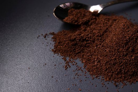 gold teaspoon in a pile of ground or instant coffee on dark background