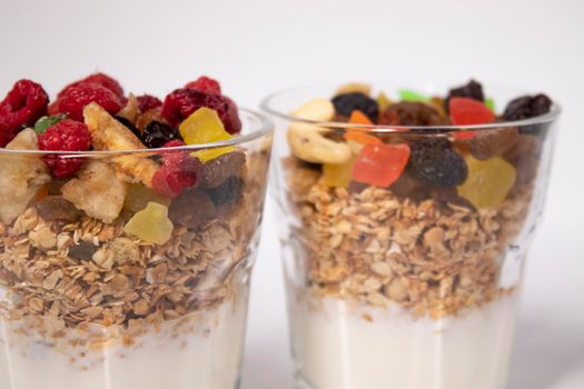 muesli dessert with yogurt and candied or dried fruits with raspberries on top in glass isolated on white background. Granola breakfast