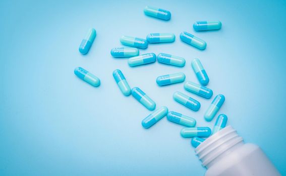 Blue antibiotic capsule pills spread out of plastic drug bottle on blue background. Antibiotic drug resistance. Antimicrobial drug overuse. Prescription drugs. Pharmaceutical industry. Health budget.