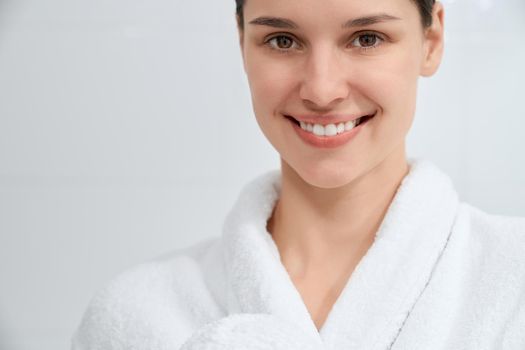 Smiling attractive woman in white robe standing in bathroom.