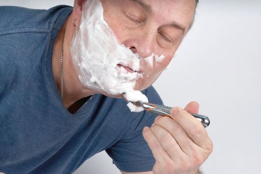 Man closing his eyes shaves with a safety razor
