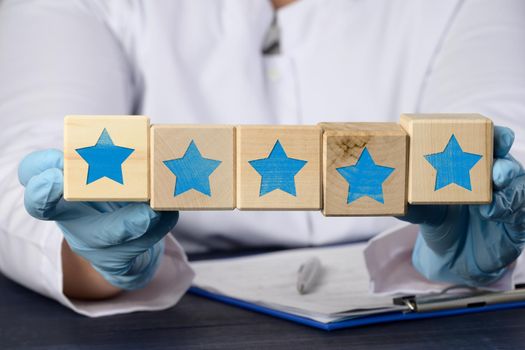 doctor in blue gloves holds cubes with five stars. Service quality assessment and rating concept