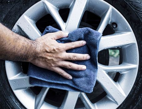 Human hand is wipe the alloy wheel of the car with a microfiber cloth