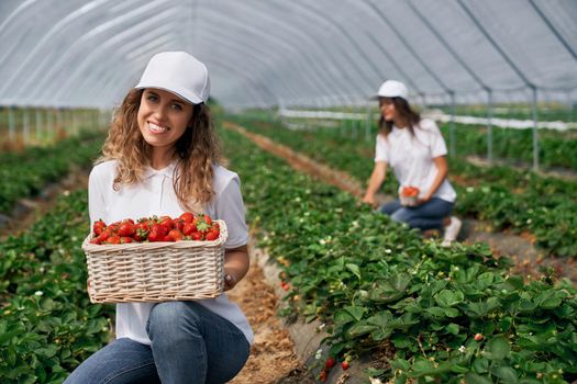Two females are posing with basket of strawberries.