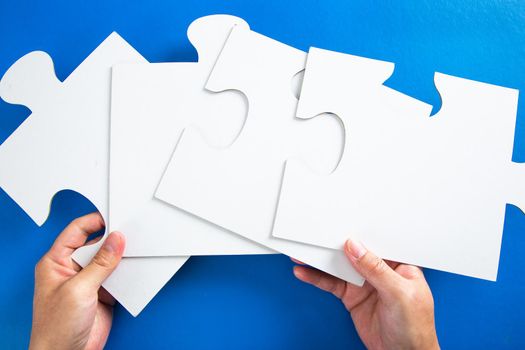 man hands holding big paper white blank puzzles on a blue background, concept of business