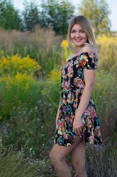 overlight bright portrait of a charming attractive blonde in flowery dress in the field