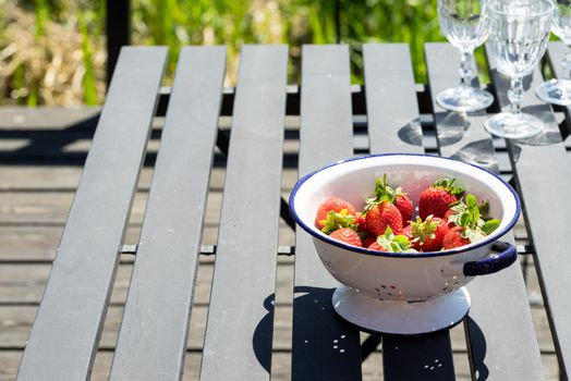 Bowl of fresh strawberries in a white bowl or colander on a black wooden table outdoors