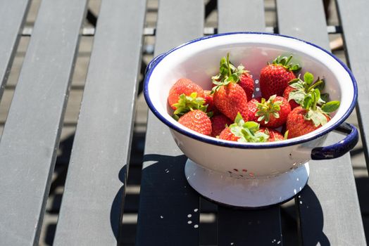 Bowl of fresh strawberries in a white bowl or colander on a black wooden table outdoors