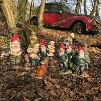 Group of stone gnome statues in an autumn forest with a old abandoned car in the background