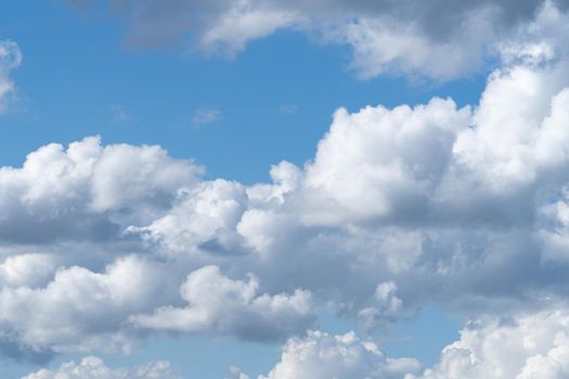 A skyscape with cumulus clouds in white and grey and a clear deep blue sky in the summer