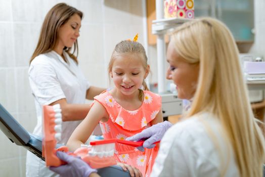 Dentist learning little girl patient how to brush her teeth with toothbrush.  