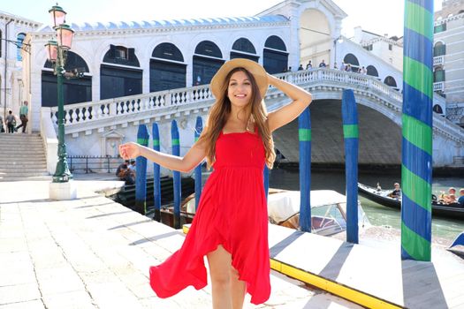 Beautiful young woman with a red dress walking in Venice near Rialto Bridge, Italy