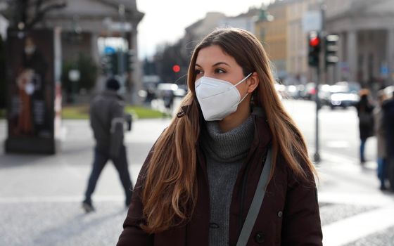 Sense of bewilderment. Young woman in winter clothes walking in street wearing protective mask FFP2 KN95. Girl with face mask feeling alone during a pandemic.
