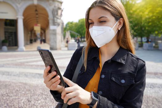 Young businesswoman wearing KN95 FFP2 face mask using her smartphone outdoors