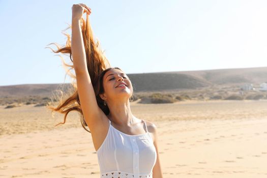 Carefree woman breathing fresh air on the beach with flying hair in the wind
