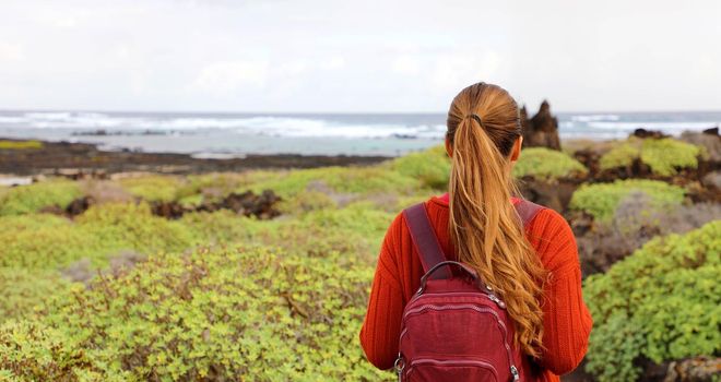 Hiking in spring time. Back view of girl exploring the northern of the island of Lanzarote, Canary Islands. Panoramic banner view of young backpacker woman discovering wild region of Lanzarote.