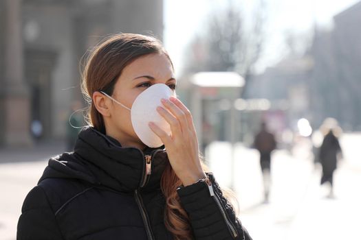 COVID-19 Young girl in city street wearing face mask protective for spreading of Coronavirus Disease 2019. Close up of young woman with surgical mask on face against SARS-CoV-2.