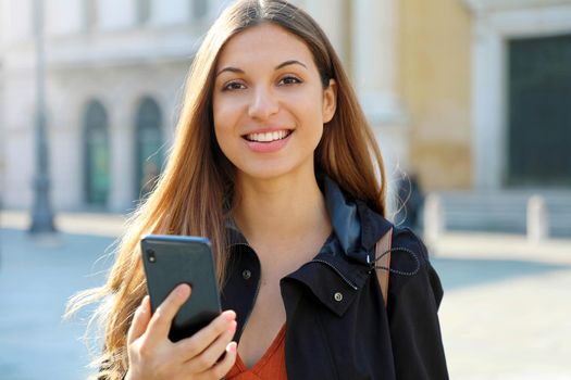 Brazilian bright cheerful student girl holding smart phone and looks at camera