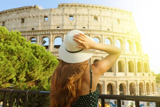 Travel in Rome. Back view of beautiful girl visiting Colosseum landmark at sunset. Summer holidays in Italy.