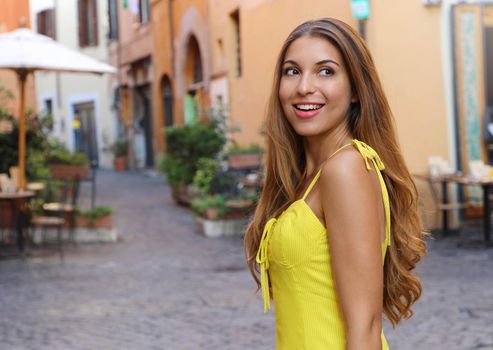 Elegant portrait of beautiful fashion woman with long hair in yellow summer dress walking in Trastevere neighborhood Rome, Italy.