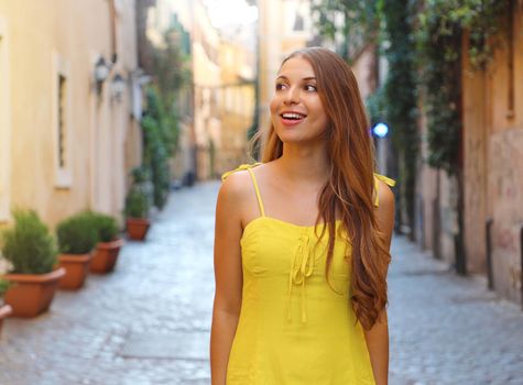 Portrait of beautiful fashion woman with long hair in yellow summer dress walking and exploring Trastevere neighborhood in Rome, Italy.