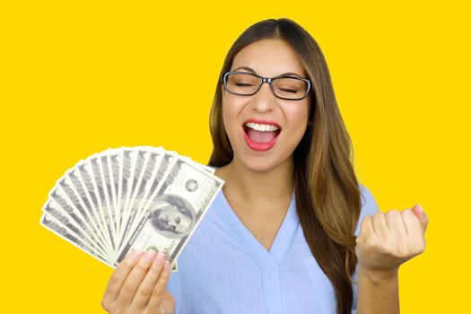 Portrait of beautiful young woman laughing and holding dollar banknotes isolated over yellow background in studio. Easy loans concept.