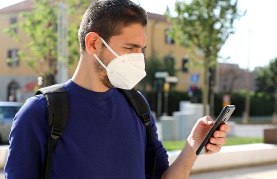 COVID-19 Mobile Application Young Man Wearing KN95 FFP2 Mask Using Smart Phone App in City Street to Aid Contact Tracing and Self Diagnostic in Response to the Coronavirus Pandemic 2019