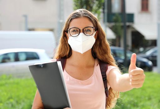Optimistic student girl back to school with protective mask shows thumb up