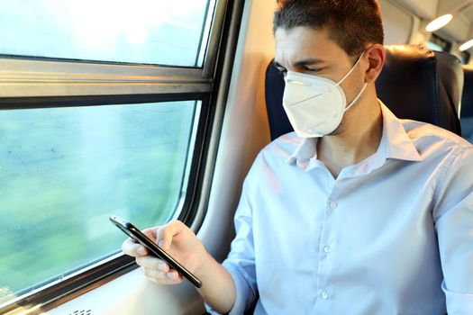 Relaxed man with KN95 FFP2 face mask using smart phone app. Train passenger with protective mask  texting on mobile phone. Travel safely on public transport.